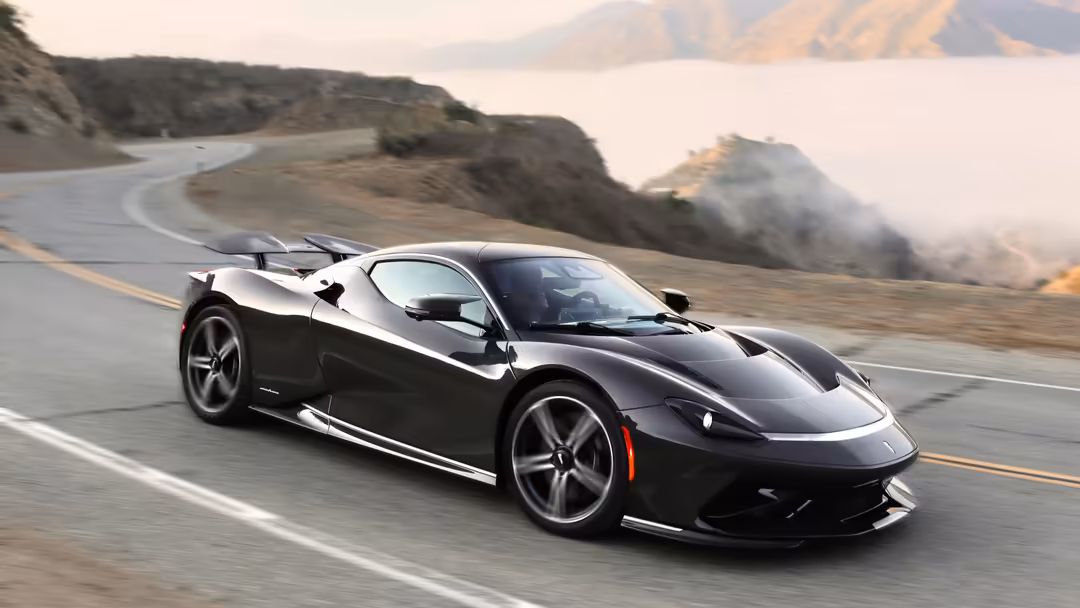 Black Pininfarina Battista supercar with open doors driving on a winding mountain road with scenic valley landscape in the ba