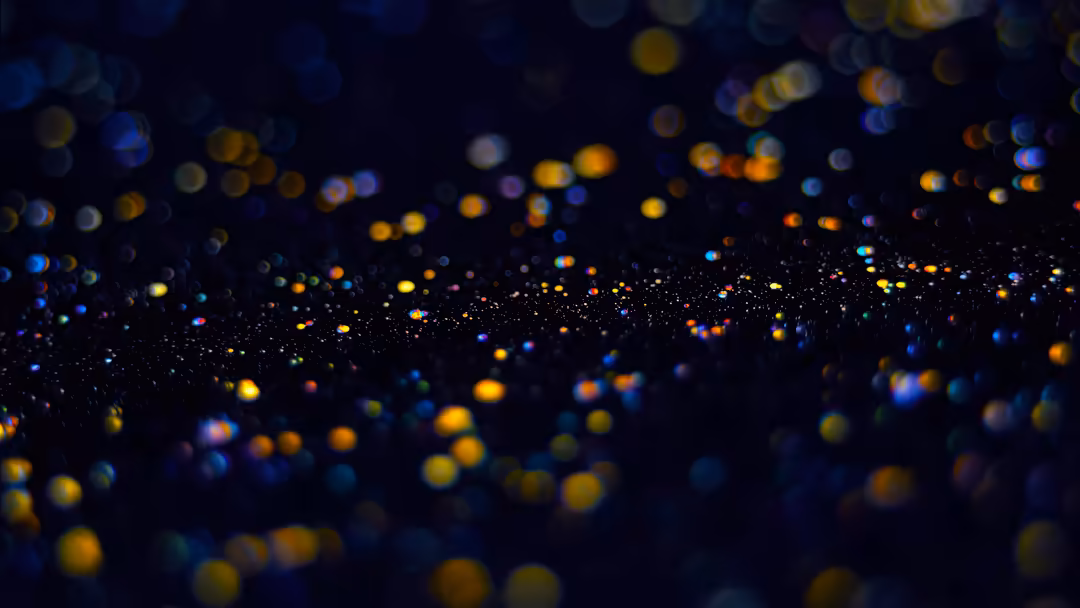 Blurred bokeh lights in warm yellow and cool blue tones scattered across a dark background, creating a dreamy abstract patter
