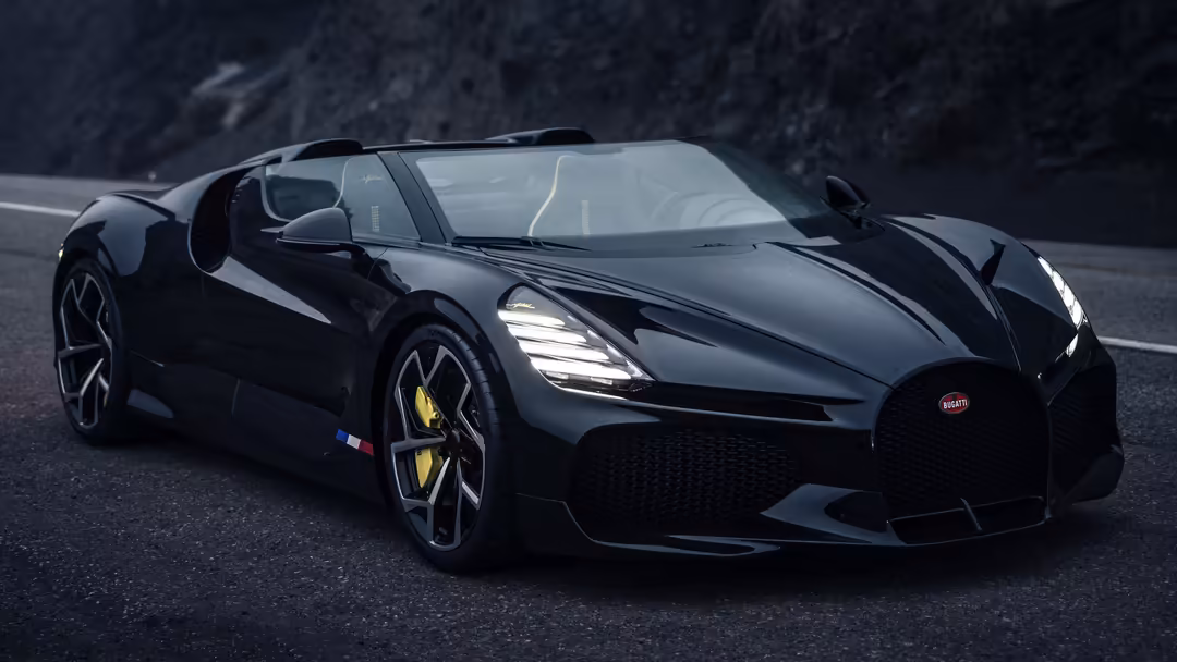 Sleek black Bugatti W16 Mistral hypercar with open doors on a curved mountain road, featuring LED headlights and gold brake c