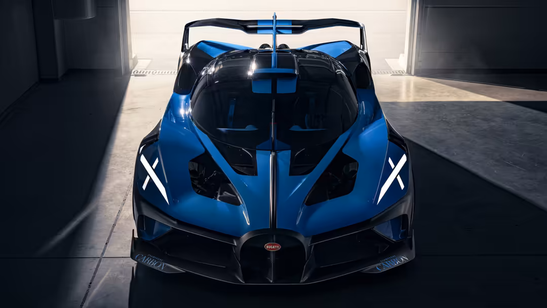 Front view of a striking blue Bugatti Bolide hypercar with white racing stripes, displayed in a modern garage with dramatic l