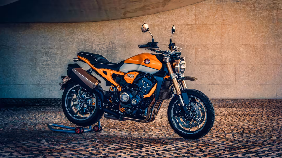 Orange and black motorcycle with chrome details parked on brick pavement against textured concrete wall backdrop