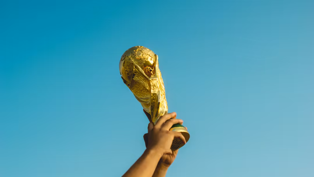 Golden FIFA World Cup trophy held high against a clear turquoise blue sky, symbolizing victory and international football cha