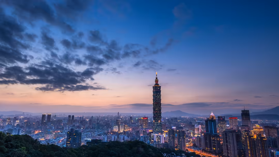 Taipei 101 tower illuminated at dusk with sprawling cityscape and purple-blue twilight sky with dramatic clouds