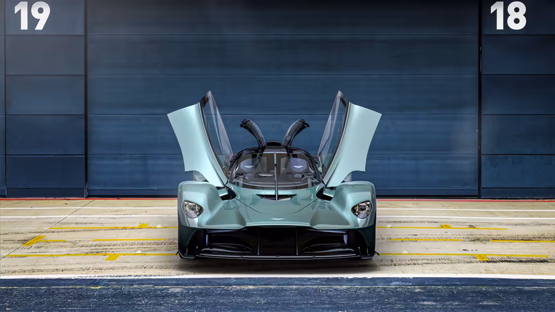 Mint green Aston Martin Valkyrie Spider hypercar with open gullwing doors displayed in front of industrial blue metal garage