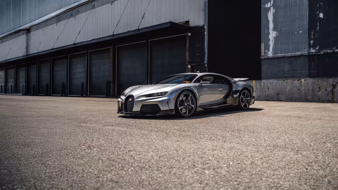 White and black Bugatti Chiron Super Sport parked in industrial warehouse with weathered metal garage doors and concrete pave