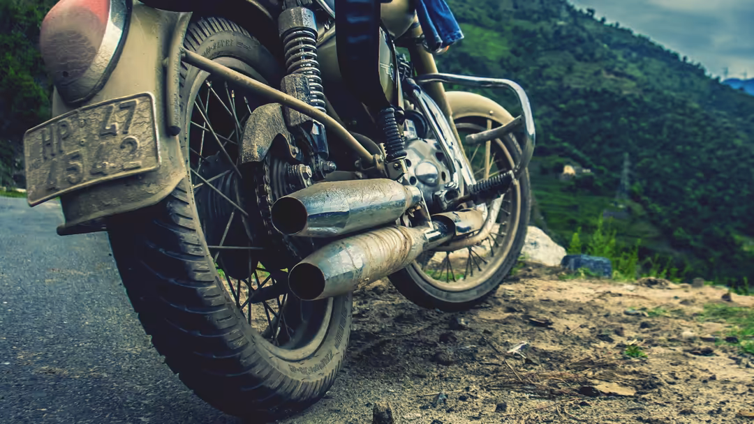 Vintage motorcycle with sidecar and weathered exhaust pipes parked on a mountain road with lush green hills in the background