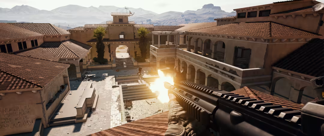 Tactical first-person shooter view of a desert compound with clay buildings, central courtyard, and mountains in the backgrou