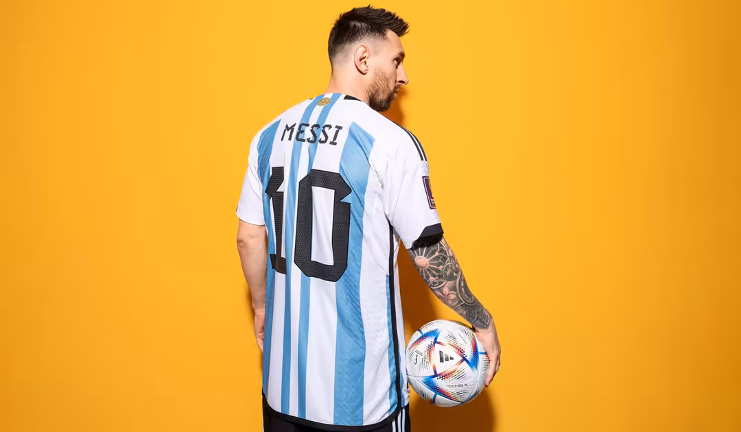 Professional athlete in striped Argentina jersey number 10 holding official World Cup soccer ball against bright yellow backg