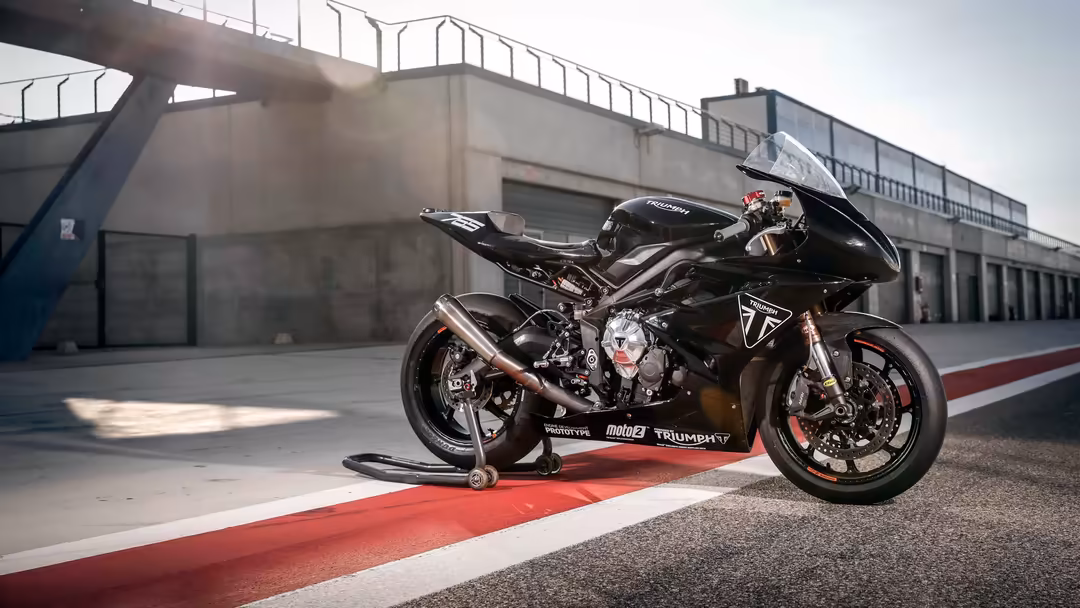 Black racing motorcycle on red pit lane at modern motorsport track with industrial buildings and pedestrian bridge in backgro