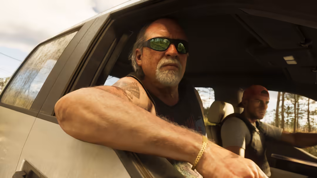 Man with sunglasses leaning out car window on open road, passenger visible inside vehicle, scenic landscape behind