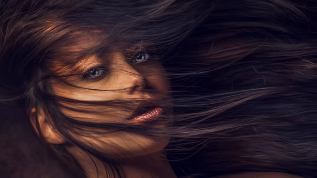 Portrait of a beautiful woman with long dark hair flowing across her face, dramatic warm lighting against dark background