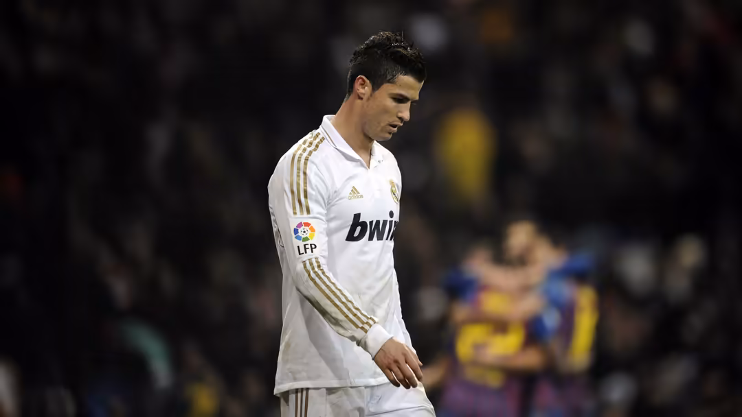 soccer player in white jersey with gold stripes and bwin sponsor walks on field with blurred crowd in dark background.