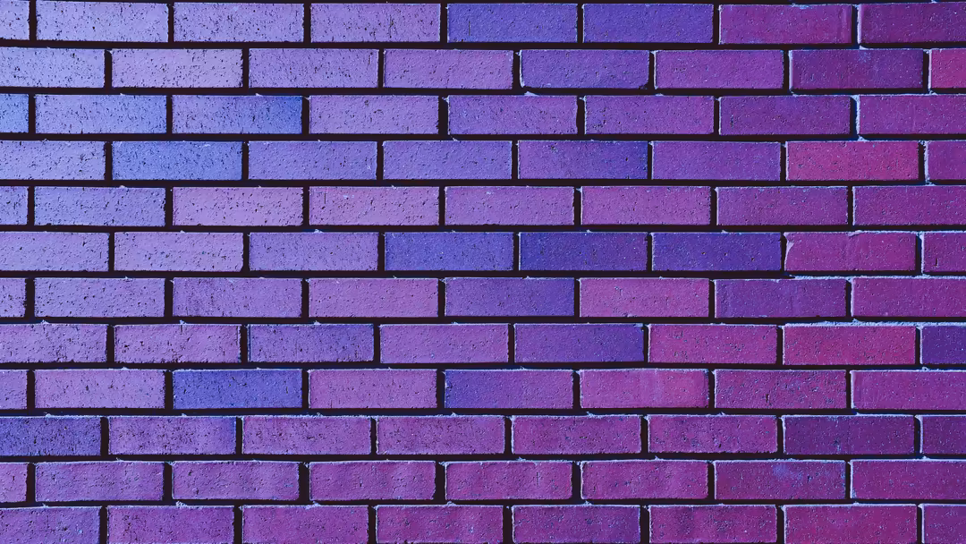 Close-up of a textured purple brick wall with dark mortar lines, displaying weathered surface and vibrant gradient coloring f