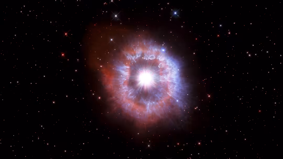 Brilliant cosmic nebula with bright central star surrounded by red and blue gas clouds against starfield backdrop