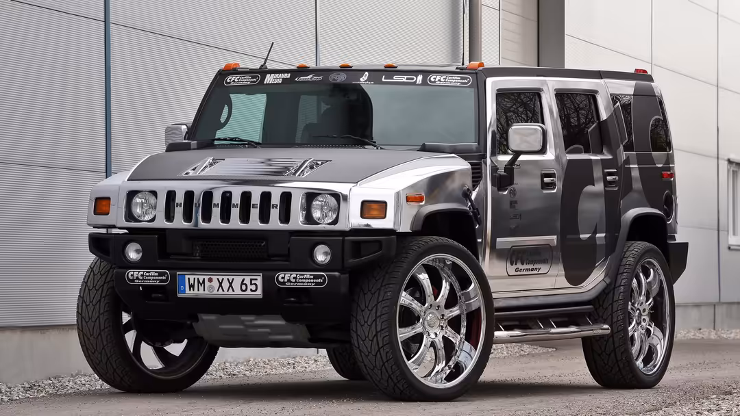 Custom modified Hummer H2 with oversized chrome wheels and lifted suspension parked against industrial metal backdrop