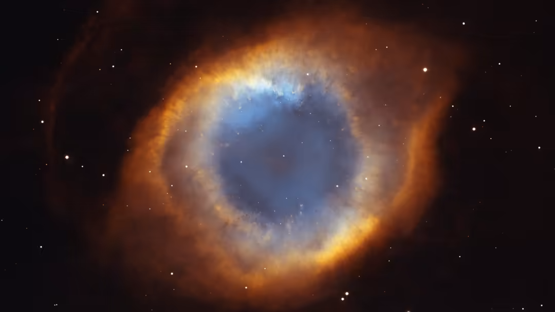 The Helix Nebula resembles a cosmic eye with blue center and golden-orange outer rings surrounded by stars in deep space