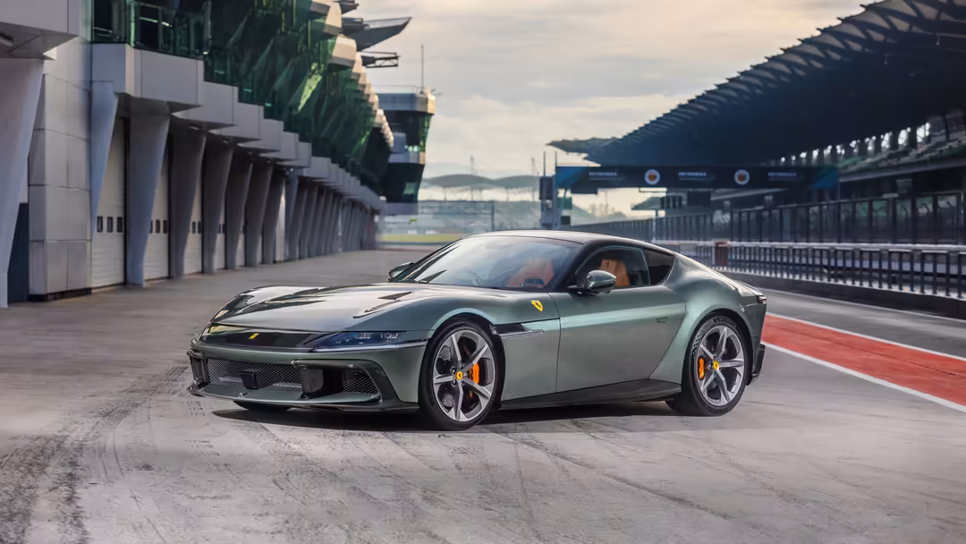 Green Ferrari 12Cilindri sports car parked on professional racing track with modern pit structures and grandstands visible in