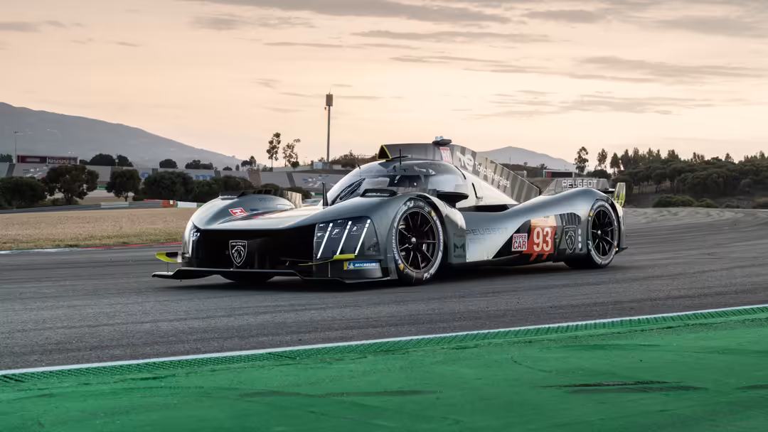 White and black Peugeot 9X8 race car with number 93 livery parked on a racing circuit with green curbing