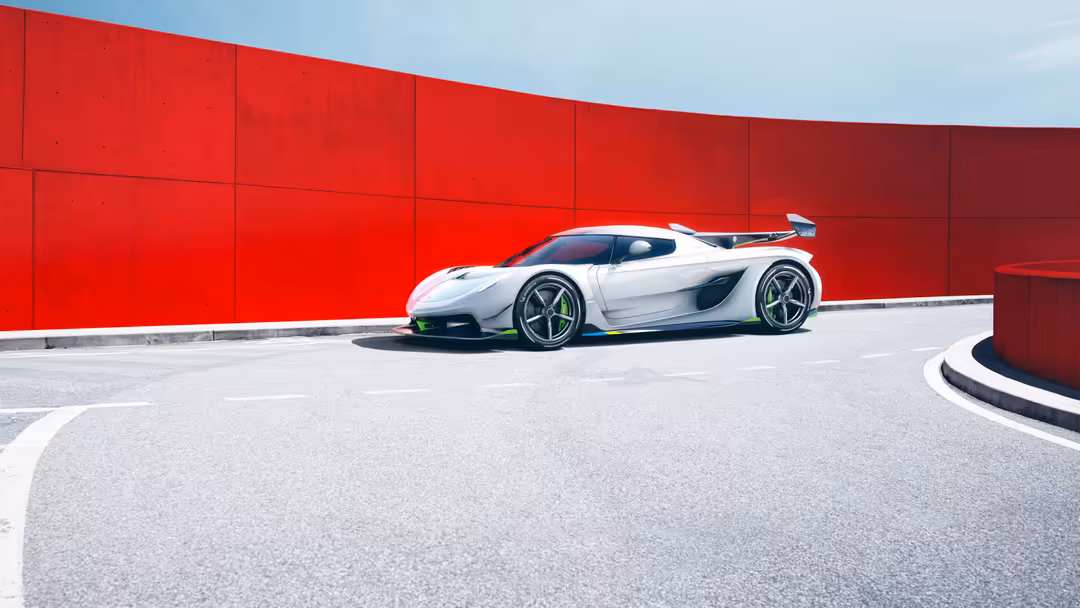 White Koenigsegg Jesko hypercar parked against a vibrant red wall with curved architectural elements and light gray pavement