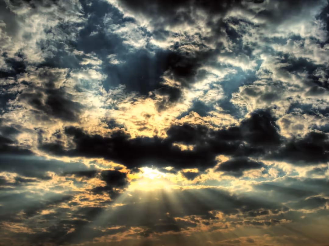 Dramatic cloudy sky with golden sunlight breaking through dark storm clouds creating ethereal light rays