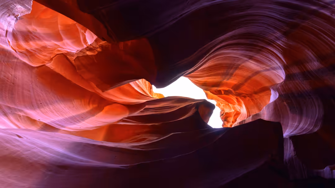 Dramatic light rays streaming through narrow slot canyon with glowing pink, orange, and purple sandstone walls creating an et