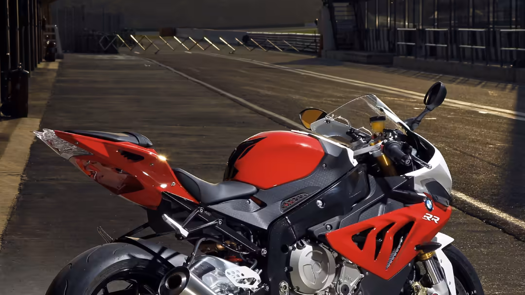 Red and black sport motorcycle parked in modern garage with dramatic sunlight casting shadows on concrete floor