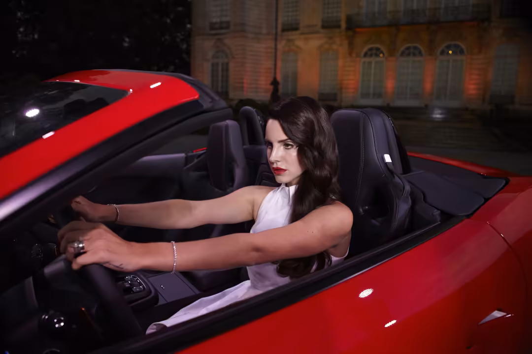 Woman with dark hair at the steering wheel of a red convertible car at night with illuminated brick building backdrop