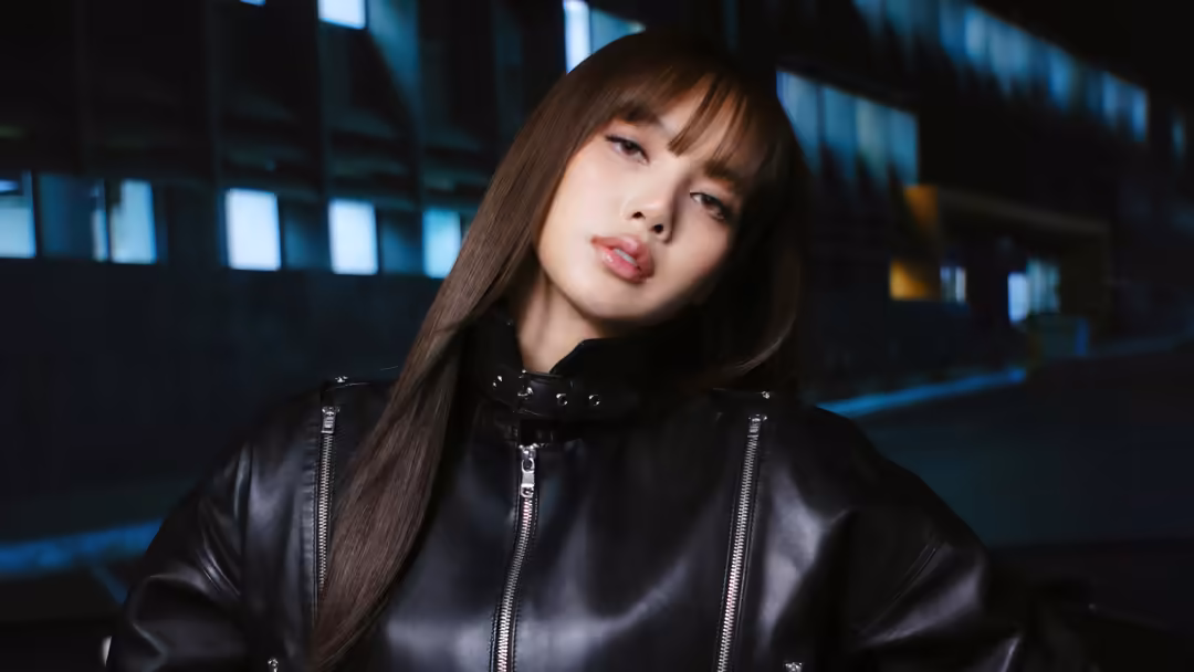 Lisa wearing black leather jacket with metal zippers in moody nighttime urban setting with blue neon building lights in backg