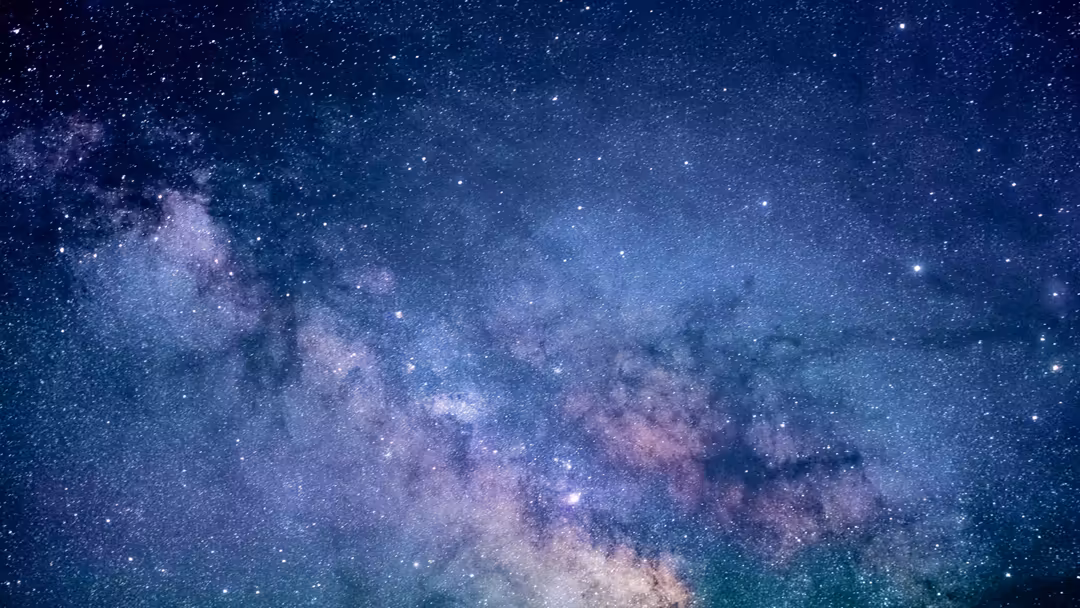 Milky Way galaxy sprawling across a deep blue starfield with purple nebula clouds and countless twinkling stars