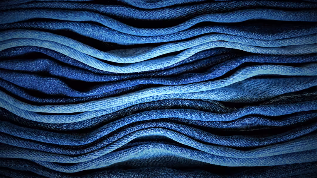 Close-up of layered blue denim fabric with wavy texture and dimensional folds creating an abstract pattern with light and sha