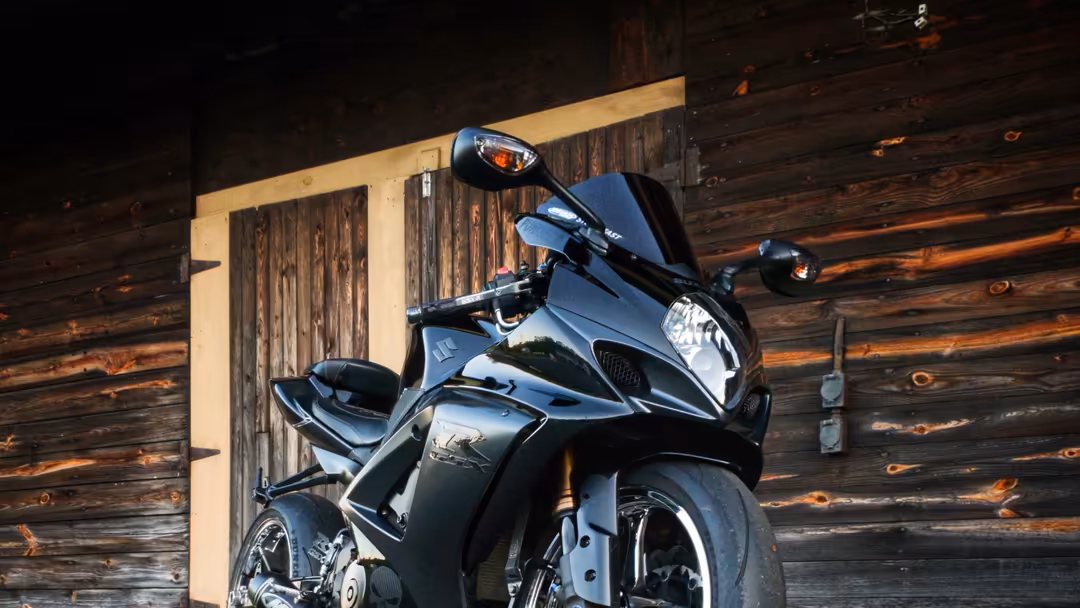 Black and silver motorcycle parked against weathered dark wooden barn wall with light wooden beam overhead