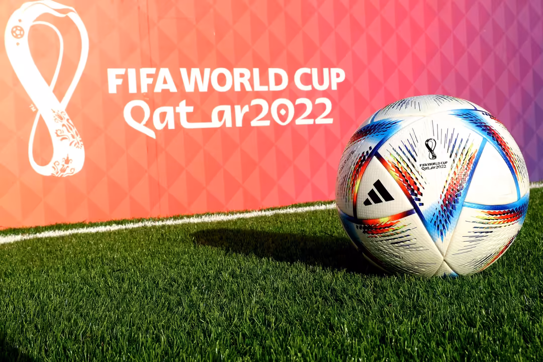 FIFA World Cup Qatar 2022 official soccer ball on grass field with tournament logo and gradient background
