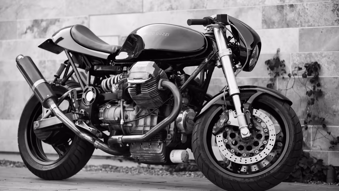 Classic café racer motorcycle with sleek black and white design, chrome details, and disc brakes displayed against a weathere