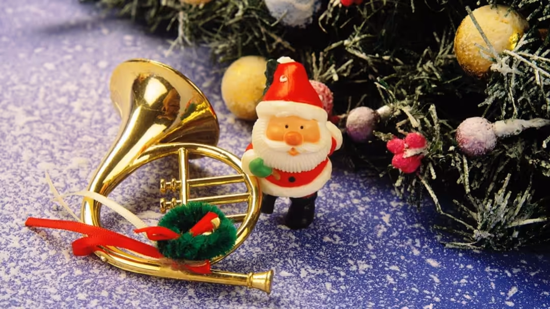 Festive holiday decorations with a golden trumpet, Santa figurine with red hat, and colorful ornaments on purple snowy backgr