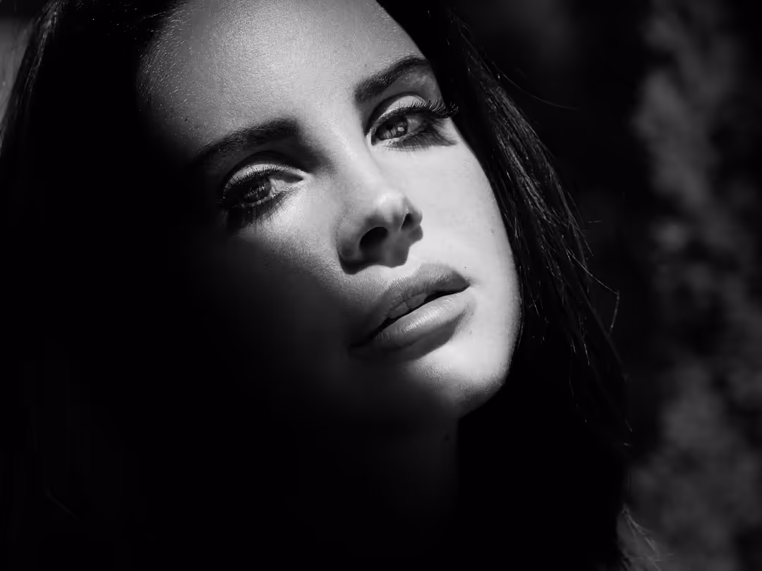 Black and white portrait of Lana Del Rey with dramatic side lighting, dark hair, defined makeup, and contemplative expression