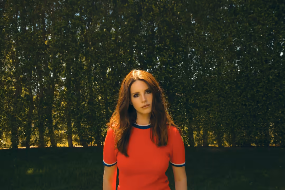 Woman with long dark hair wearing a red shirt standing against a textured green and gold background with natural lighting
