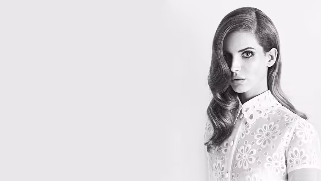Black and white portrait of Lana Del Rey wearing a delicate lace white top, photographed in profile with long flowing hair ag