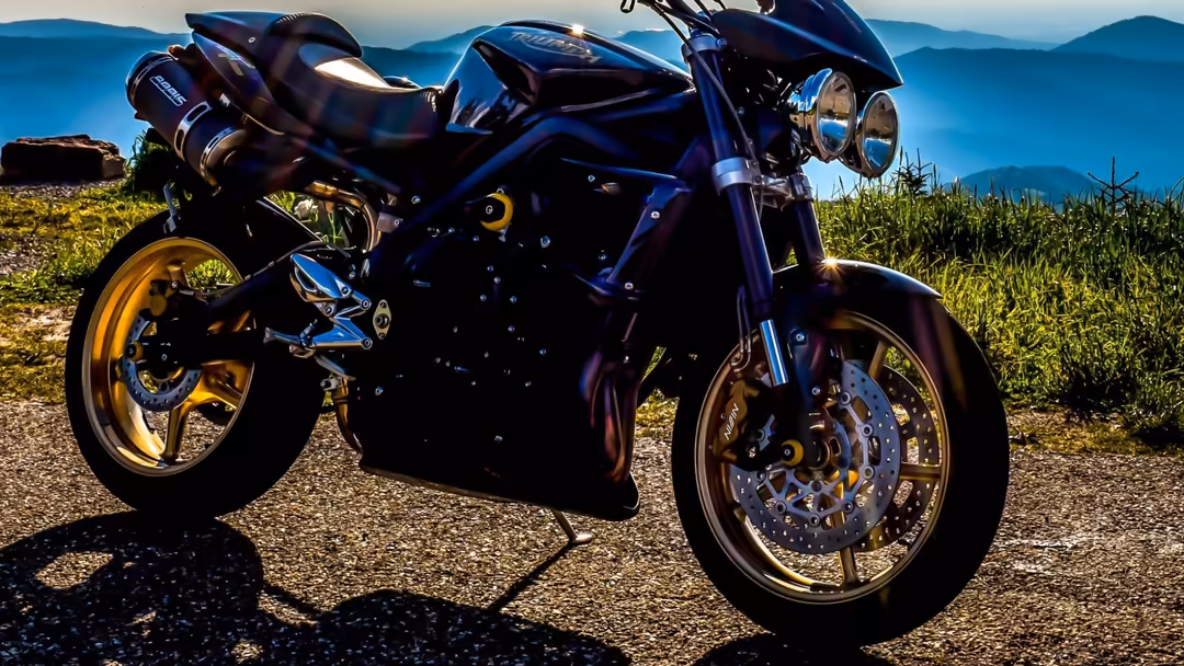 Custom motorcycle with blue frame and gold wheels parked on dirt road with mountains and green fields in scenic background
