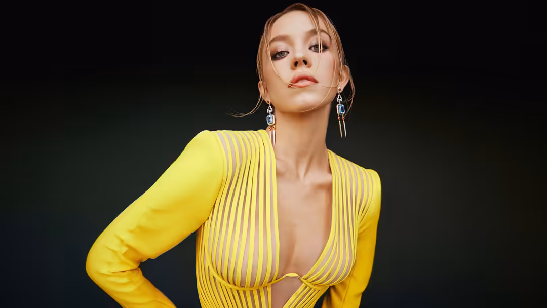 Woman in vibrant neon yellow pleated dress with statement silver earrings against dark background, showcasing modern fashion