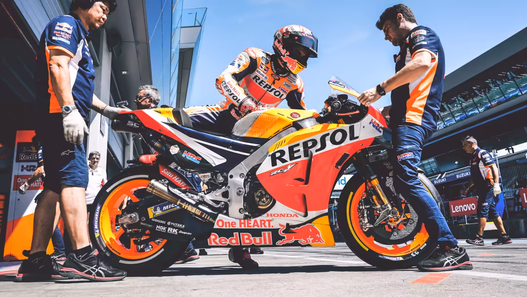 MotoGP racing bike with Repsol and Red Bull branding surrounded by pit crew team members in blue uniforms during maintenance
