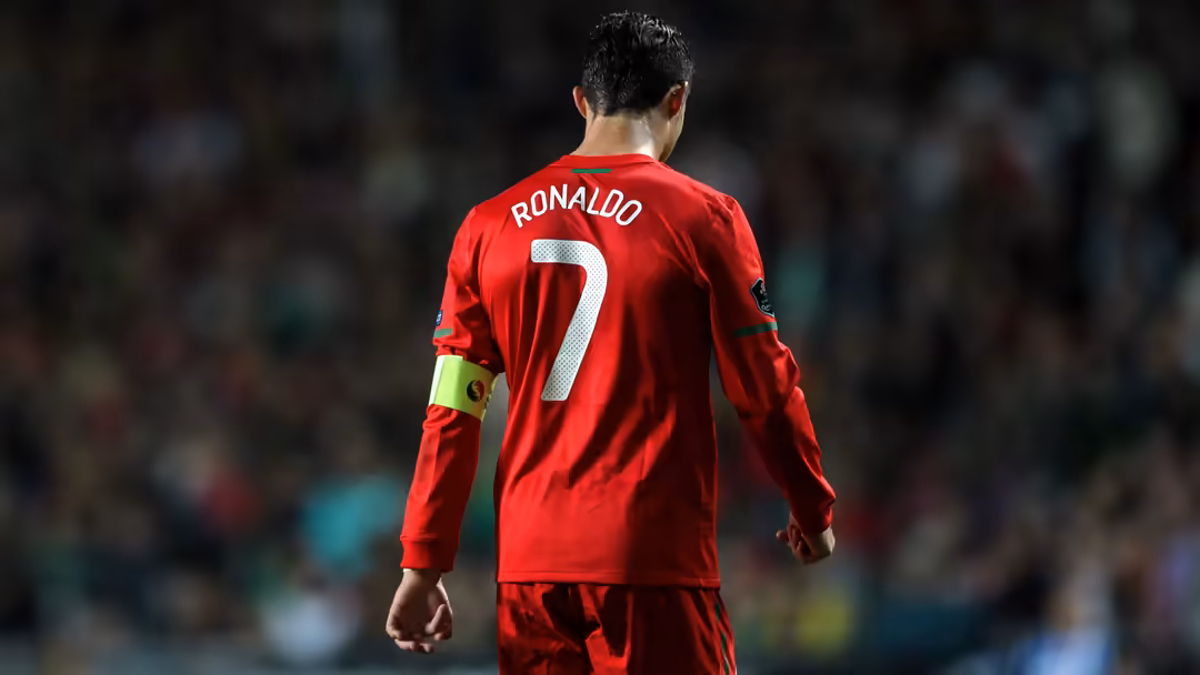 soccer player wearing bright red jersey number 7 with captain's armband, photographed from behind on a blurred stadium…