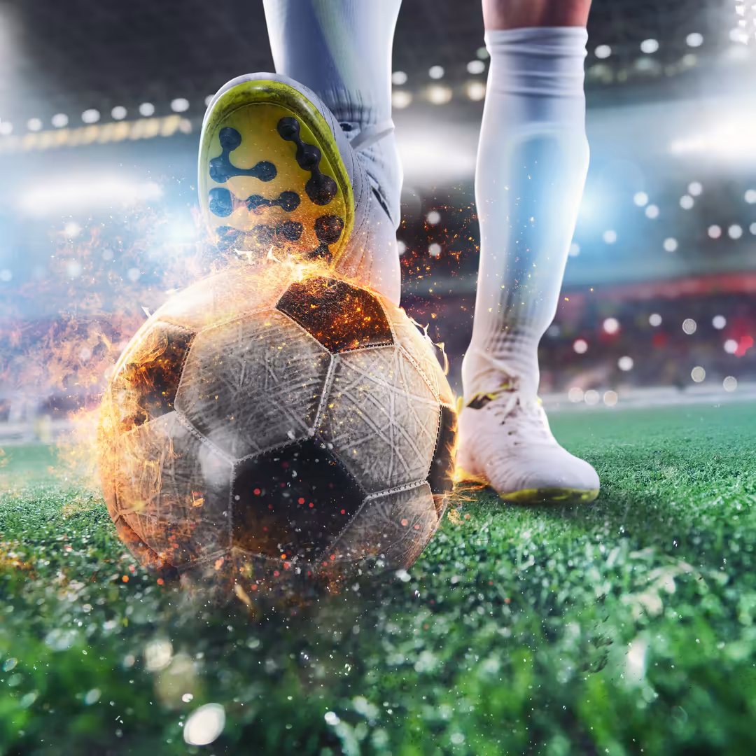 Soccer player in white socks about to kick a flaming ball with yellow cleats on stadium grass with bokeh lights