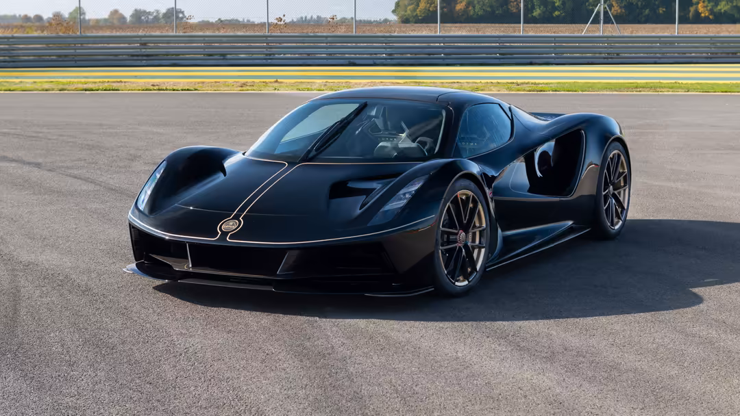 Black Lotus Evija hypercar parked on racing track with open door, showing sleek aerodynamic design and professional motorspor