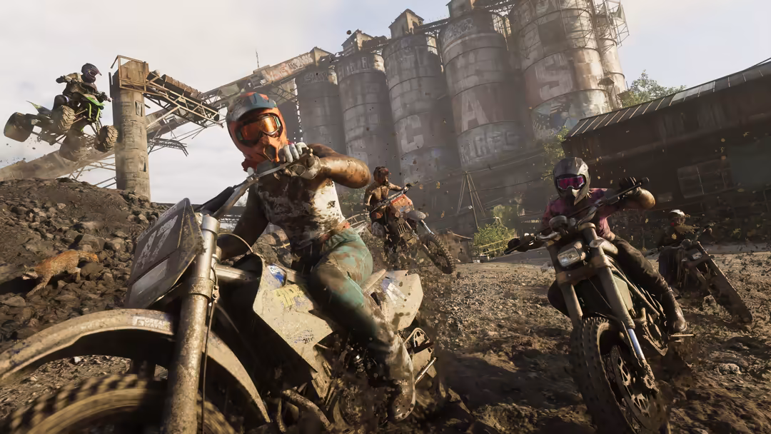 Players on dirt bikes in a post-apocalyptic wasteland with industrial silos and ruins in the background during gameplay