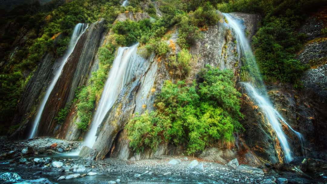 Multiple tiered waterfalls cascade down moss-covered rocky cliffs surrounded by vibrant green vegetation and lush foliage in