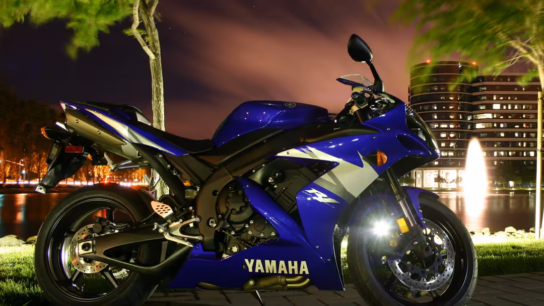 Blue and white sport bike parked at night with illuminated city buildings and park landscape in background