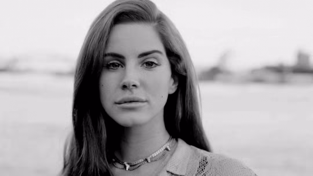 Black and white portrait of Lana Del Rey with long dark hair, wearing a necklace, gazing thoughtfully with a blurred water ba