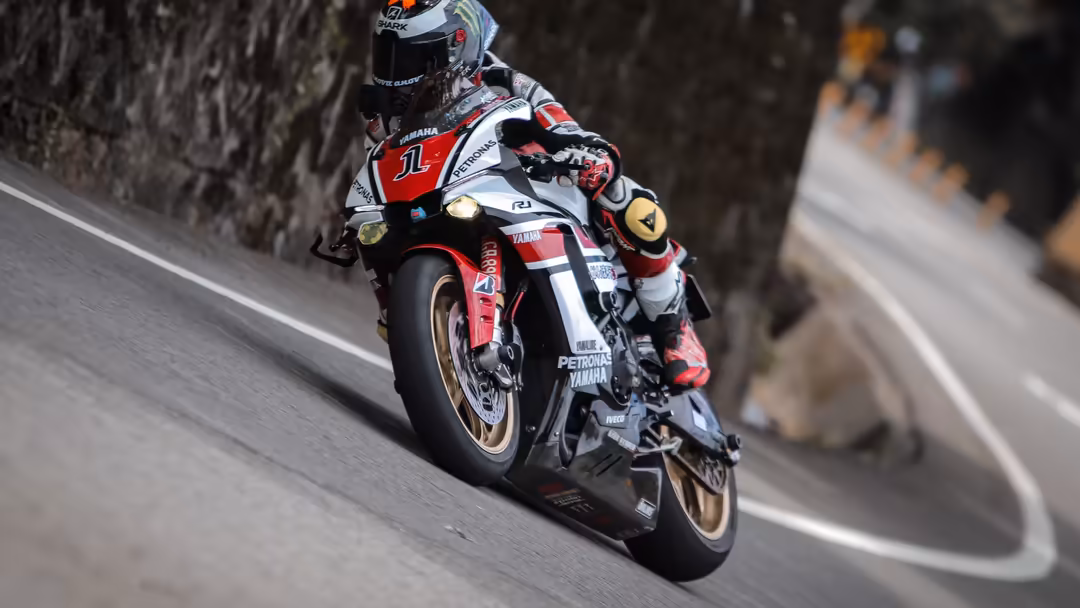 Professional motorcycle racer in red and white Yamaha sportbike leaning into a high-speed turn on a track with stone walls.