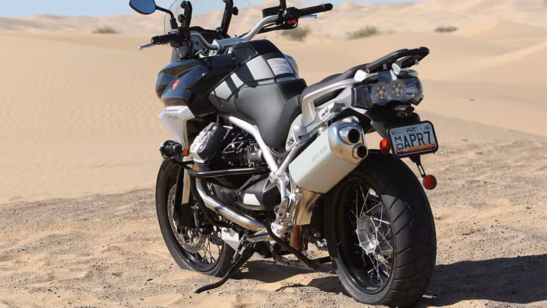 Sleek motorcycle with chrome accents parked on sandy desert terrain under bright sunlight with dunes in background