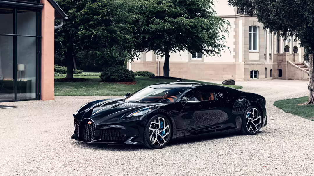 Sleek black Bugatti La Voiture Noire hypercar parked on gravel driveway with modern architecture and manicured lawn in backgr